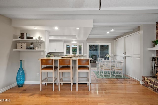 kitchen with kitchen peninsula, white cabinets, a kitchen bar, and light hardwood / wood-style floors