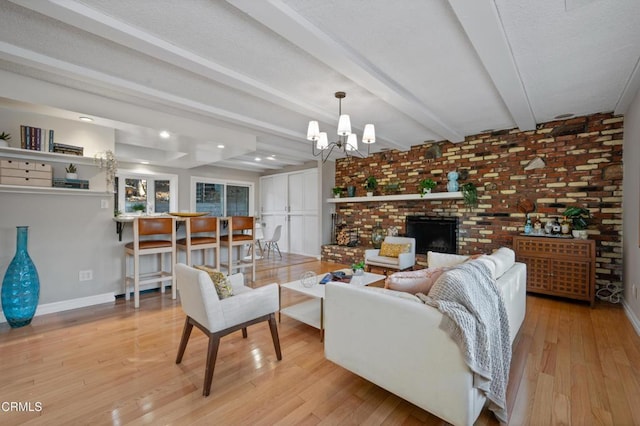 living room featuring beamed ceiling, a fireplace, a chandelier, brick wall, and light hardwood / wood-style flooring