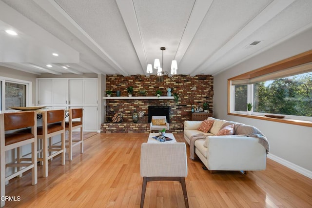 living room featuring light hardwood / wood-style flooring, a fireplace, brick wall, an inviting chandelier, and beamed ceiling