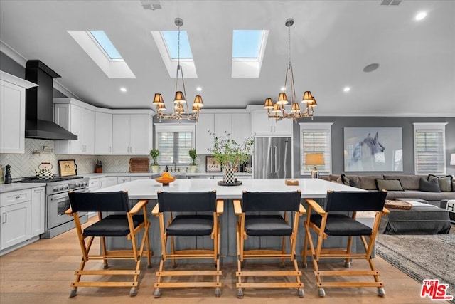 kitchen featuring decorative light fixtures, premium appliances, wall chimney range hood, and a notable chandelier