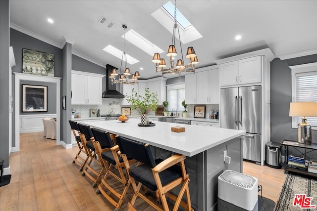 kitchen featuring white cabinets, vaulted ceiling with skylight, a breakfast bar, wall chimney range hood, and stainless steel appliances