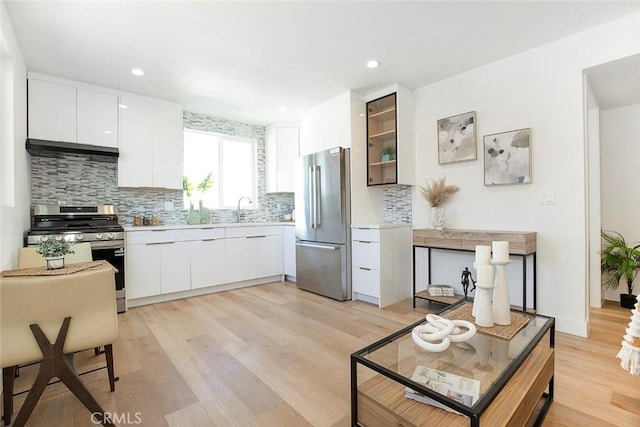 kitchen with white cabinets, stainless steel appliances, light hardwood / wood-style floors, sink, and range hood