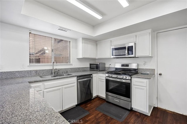 kitchen with light stone countertops, appliances with stainless steel finishes, white cabinetry, sink, and dark hardwood / wood-style floors