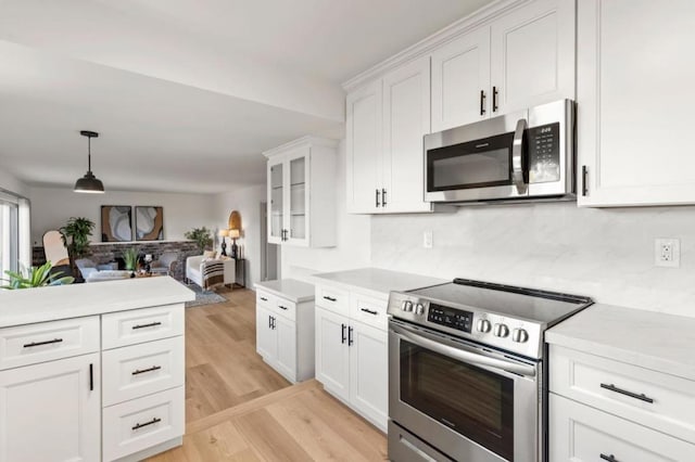 kitchen with pendant lighting, appliances with stainless steel finishes, light wood-type flooring, white cabinetry, and tasteful backsplash