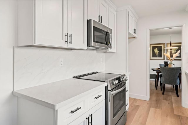 kitchen featuring white cabinets, decorative light fixtures, stainless steel appliances, tasteful backsplash, and light hardwood / wood-style flooring