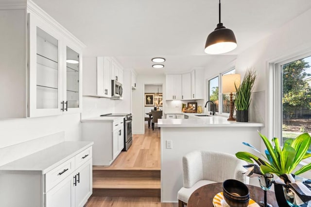 kitchen featuring kitchen peninsula, white cabinetry, hanging light fixtures, and appliances with stainless steel finishes