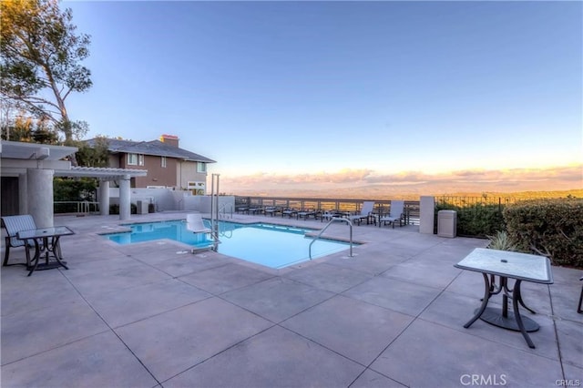 pool at dusk featuring a pergola and a patio area