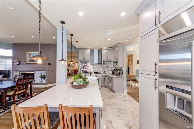 kitchen featuring gray cabinetry, appliances with stainless steel finishes, a kitchen island, pendant lighting, and wall chimney range hood