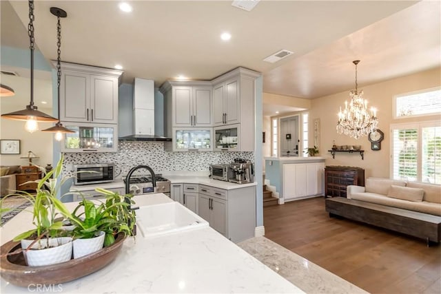 kitchen featuring pendant lighting, dark wood-type flooring, appliances with stainless steel finishes, backsplash, and wall chimney exhaust hood