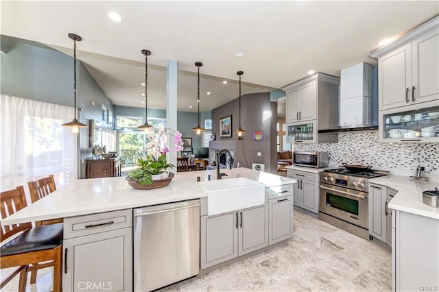 kitchen featuring wall chimney range hood, gray cabinets, a kitchen breakfast bar, and appliances with stainless steel finishes