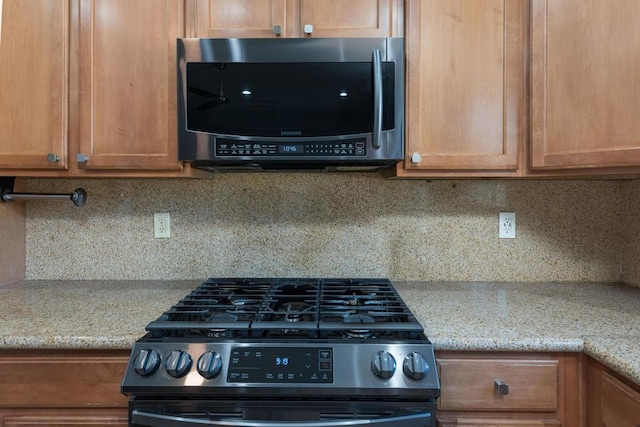 kitchen with light stone counters, decorative backsplash, and appliances with stainless steel finishes