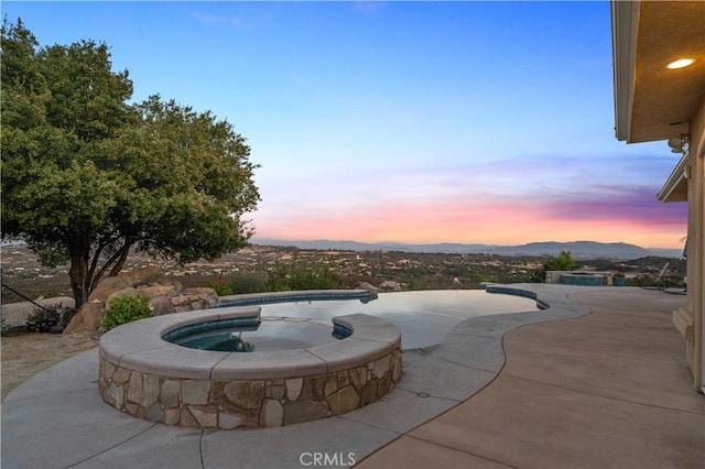 pool at dusk featuring a mountain view, an in ground hot tub, and a patio