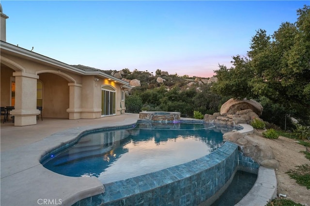 pool at dusk featuring an in ground hot tub and a patio area