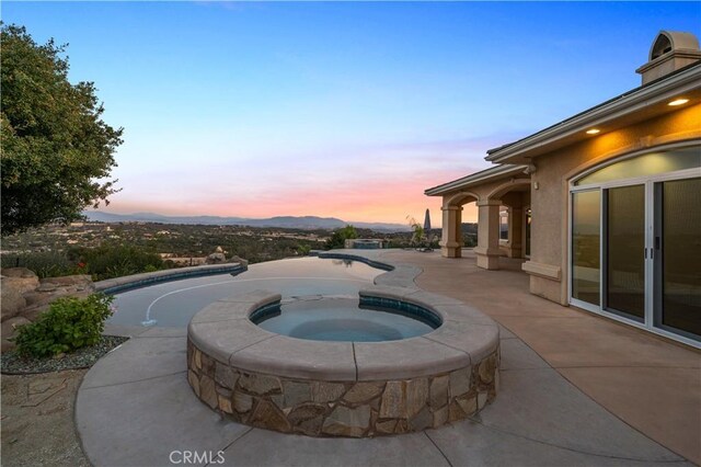 pool at dusk with a mountain view, an in ground hot tub, and a patio area