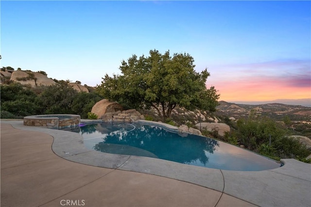 pool at dusk featuring an in ground hot tub, a mountain view, and a patio area