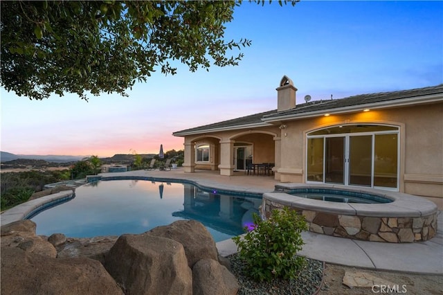 pool at dusk featuring an in ground hot tub and a patio