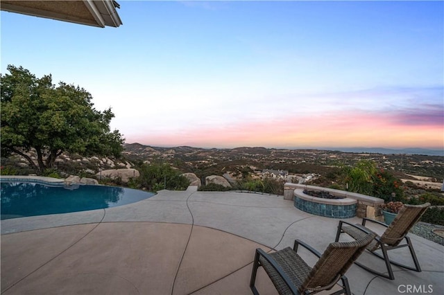 pool at dusk with a patio area and a fire pit