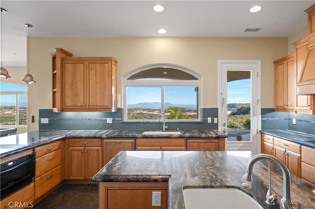 kitchen featuring sink, decorative light fixtures, dark stone counters, and oven