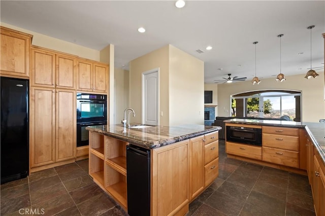 kitchen featuring black appliances, decorative light fixtures, dark stone countertops, sink, and a center island with sink