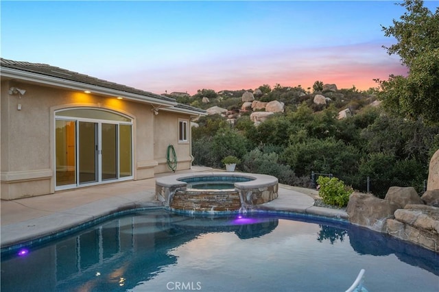 pool at dusk with an in ground hot tub, a patio, and pool water feature