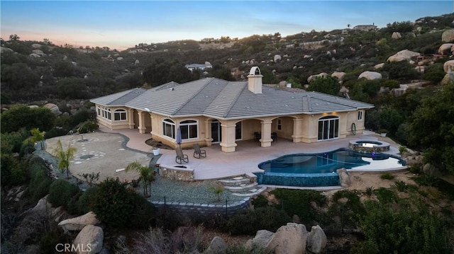 back house at dusk featuring a pool with hot tub and a patio