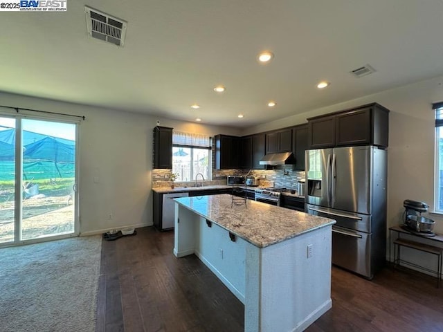 kitchen featuring dark hardwood / wood-style flooring, sink, light stone counters, a kitchen island, and stainless steel appliances