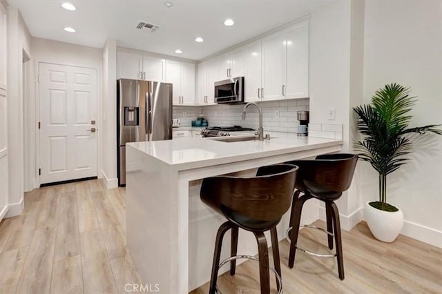 kitchen with kitchen peninsula, sink, white cabinets, a breakfast bar, and stainless steel appliances