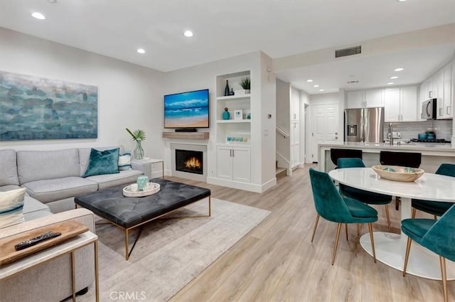 living room with sink, built in features, and light hardwood / wood-style flooring