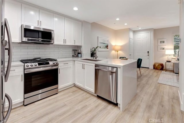 kitchen featuring kitchen peninsula, appliances with stainless steel finishes, sink, white cabinetry, and light hardwood / wood-style floors