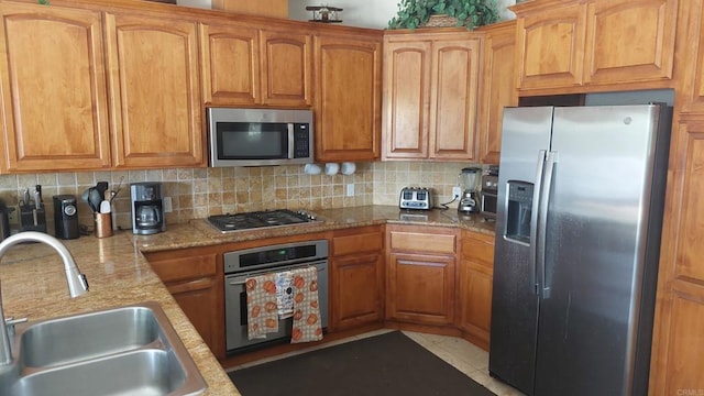 kitchen with appliances with stainless steel finishes, brown cabinetry, a sink, and backsplash