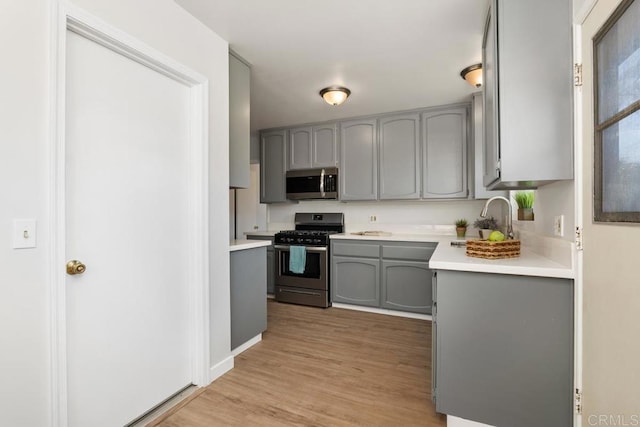 kitchen featuring sink, light wood-type flooring, gray cabinetry, and appliances with stainless steel finishes