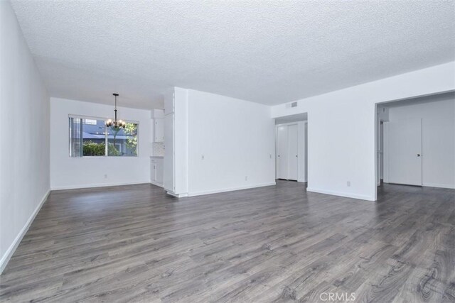 unfurnished living room featuring a textured ceiling, a notable chandelier, and dark hardwood / wood-style flooring