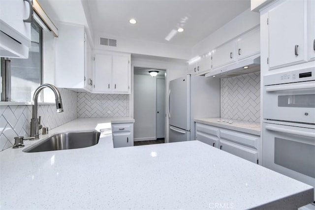 kitchen with white appliances, visible vents, decorative backsplash, white cabinetry, and a sink