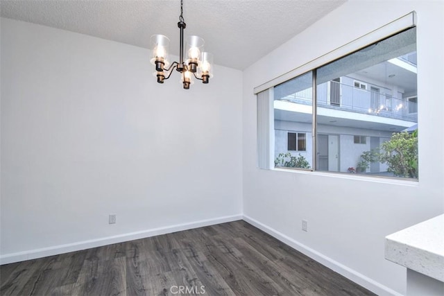 spare room featuring a notable chandelier, dark wood-type flooring, and a textured ceiling