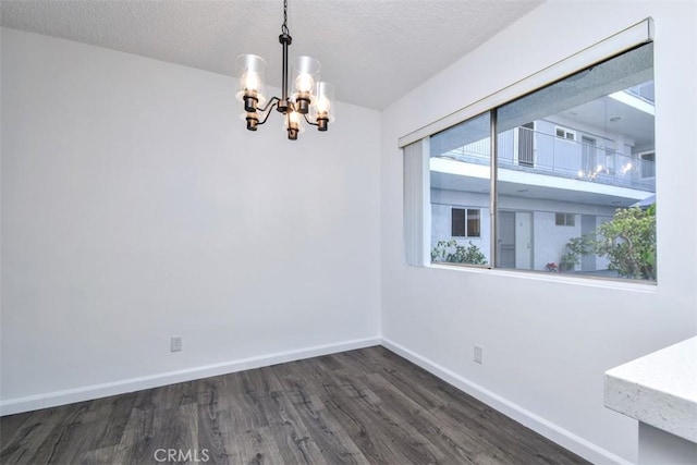 unfurnished room featuring a textured ceiling, dark wood-type flooring, a chandelier, and baseboards