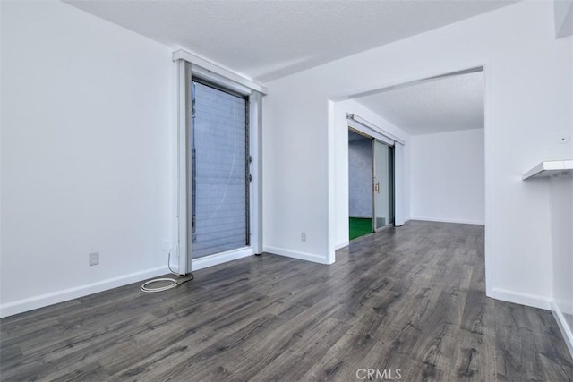 spare room featuring a textured ceiling, baseboards, and dark wood-type flooring