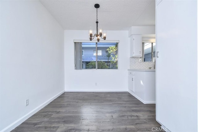 unfurnished dining area with a textured ceiling, dark hardwood / wood-style floors, and a chandelier