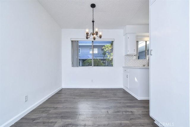 unfurnished dining area featuring a notable chandelier, a textured ceiling, baseboards, and dark wood-type flooring