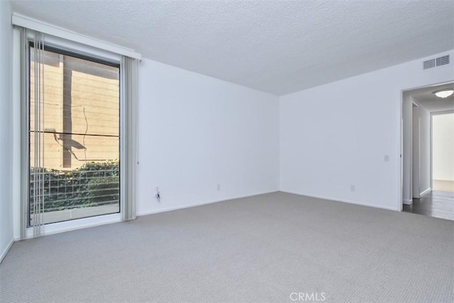 empty room with a textured ceiling, dark colored carpet, visible vents, and floor to ceiling windows