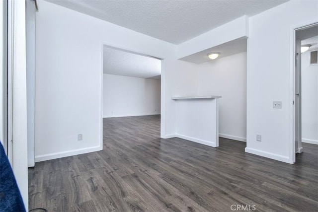 spare room featuring visible vents, a textured ceiling, baseboards, and dark wood-style flooring