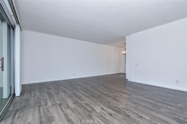 empty room with an inviting chandelier, baseboards, dark wood finished floors, and a textured ceiling