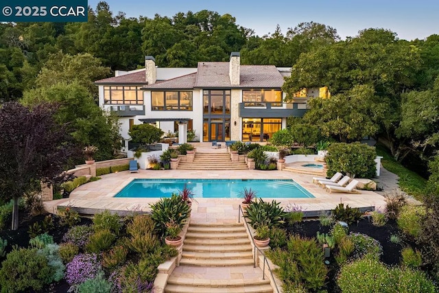 rear view of property with a balcony, a swimming pool with hot tub, and a patio area