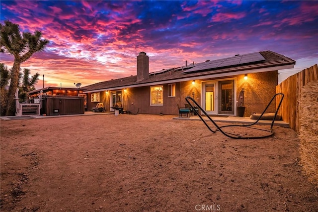 back house at dusk with a patio area, a hot tub, and solar panels