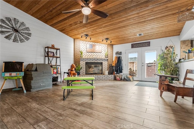 playroom featuring hardwood / wood-style floors, wood ceiling, french doors, a fireplace, and ceiling fan