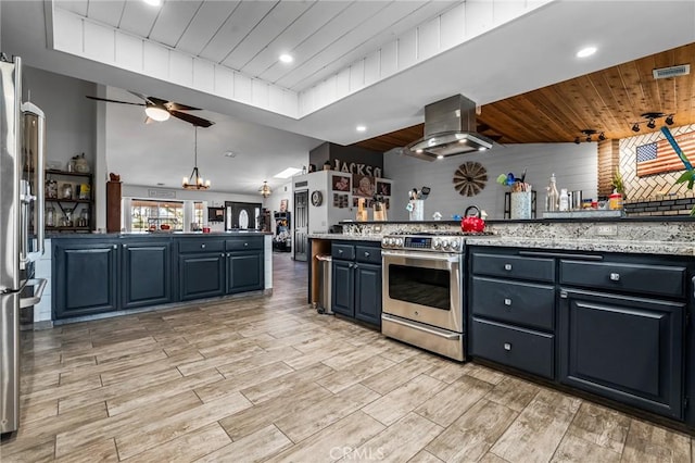 kitchen with appliances with stainless steel finishes, hanging light fixtures, island range hood, ceiling fan with notable chandelier, and light stone counters