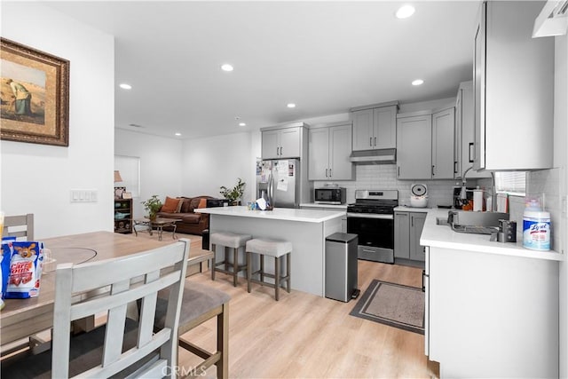 kitchen with appliances with stainless steel finishes, a kitchen island, tasteful backsplash, gray cabinetry, and a breakfast bar area