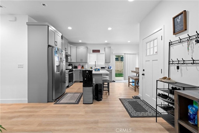 kitchen with light hardwood / wood-style flooring, appliances with stainless steel finishes, gray cabinetry, a center island, and a breakfast bar area