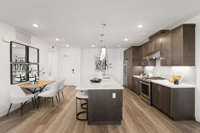 kitchen with light hardwood / wood-style flooring, a breakfast bar, hanging light fixtures, a center island, and premium appliances