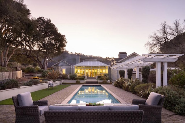 pool at dusk with a pergola, an outdoor hangout area, and a patio