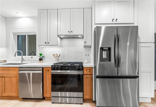 kitchen featuring backsplash, under cabinet range hood, light countertops, appliances with stainless steel finishes, and a sink